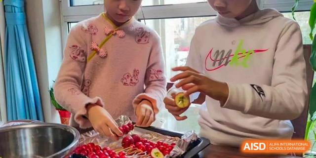 A close-up of a young girl's hands cutting or preparing apples and other fresh produce on a table for a healthy eating activity, at Beijing SMIC Private School.