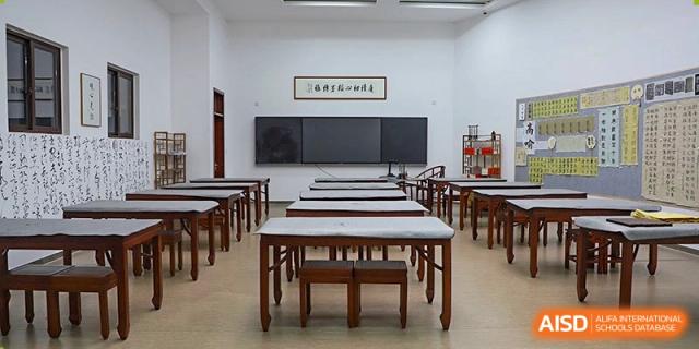 A traditional classroom at Boya International Academy (BIA) with rows of wooden desks and a large chalkboard at the front.