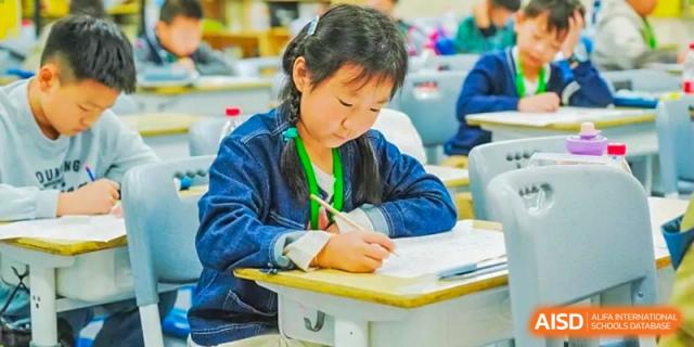 A female student from Boya International Academy (BIA) wearing a denim jacket, focused on writing or taking notes at her desk during class.