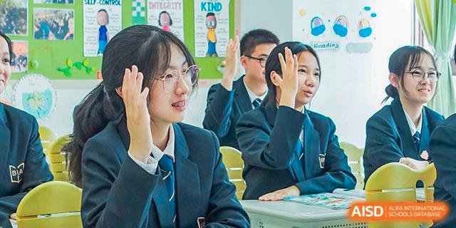 Two female students from Boya International Academy (BIA), wearing school uniforms, enthusiastically raising their hands to answer a question in class.
