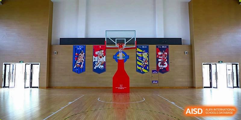 The gymnasium at Boya International Academy (BIA) featuring a wooden floor, basketball hoop, and colorful banners on the wall.