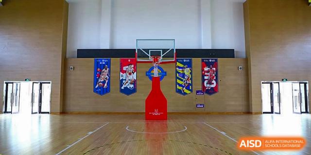 The gymnasium at Boya International Academy (BIA) featuring a wooden floor, basketball hoop, and colorful banners on the wall.