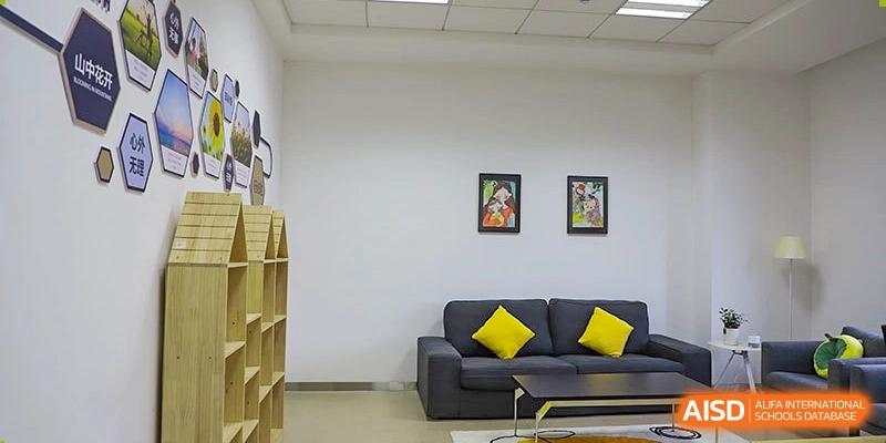 A simple, comfortable lounge or waiting area at Boya International Academy (BIA) with a gray sofa, yellow pillows, and framed artwork.