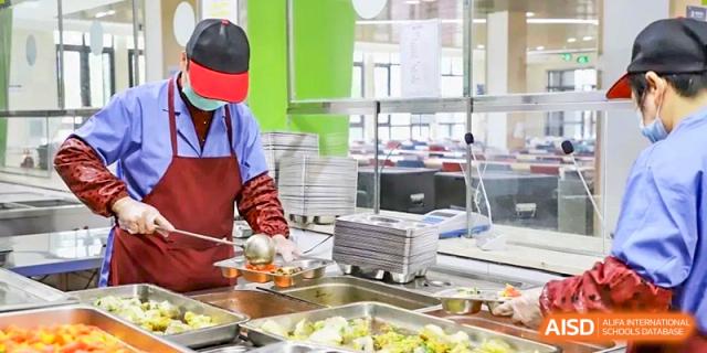 Cafeteria staff at Boya International Academy (BIA) wearing masks and gloves, preparing or serving food from the school's buffet line.