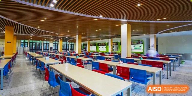 A wide view of the modern and spacious dining hall or cafeteria at Boya International Academy (BIA), featuring long tables and red and blue seating.