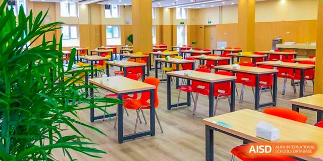An empty, brightly lit dining hall or large classroom with many red chairs and small wooden tables, Brilliant Light School SJZ.