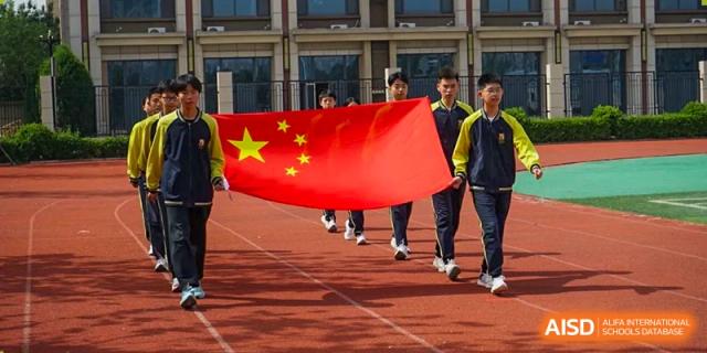 Students and teachers marching on a track, carrying the large national flag of China during a sports day or parade, Brilliant Light School SJZ.