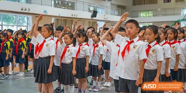 A row of students in white shirts, dark skirts, and red scarves standing and raising their right hands in a salute or pledge, Brilliant Light School SJZ.