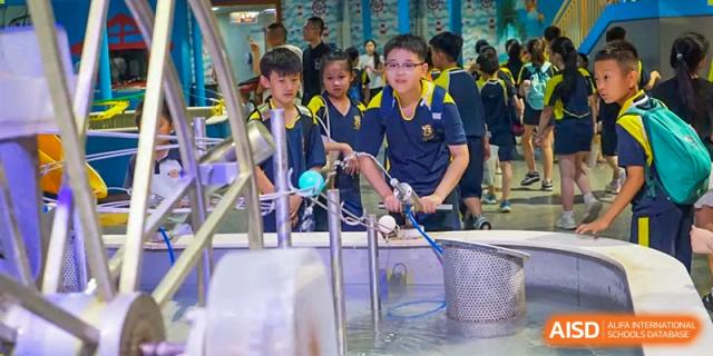 A student wearing a blue and yellow uniform conducting a science experiment involving water and a large metal basin, Brilliant Light School SJZ.