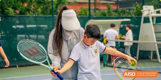 A teacher or coach helping a young male student practice a tennis swing outdoors at Brilliant Light School SJZ.
