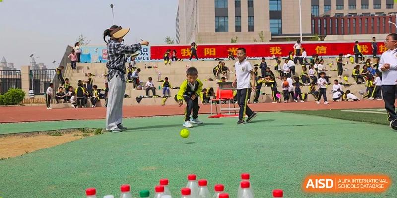 A student kicking a yellow ball toward a row of plastic bottles in an outdoor game during a school event at Brilliant Light School SJZ.