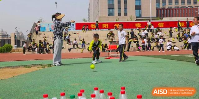 A student kicking a yellow ball toward a row of plastic bottles in an outdoor game during a school event at Brilliant Light School SJZ.