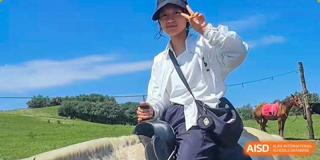 Student wearing a white shirt and dark hat posing outdoors under a clear blue sky, Brilliant Light School SJZ.