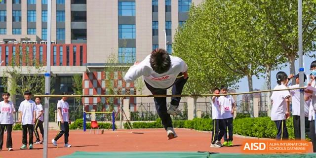 A student performing a high jump over a bar during an athletics event on a red track, Brilliant Light School SJZ.