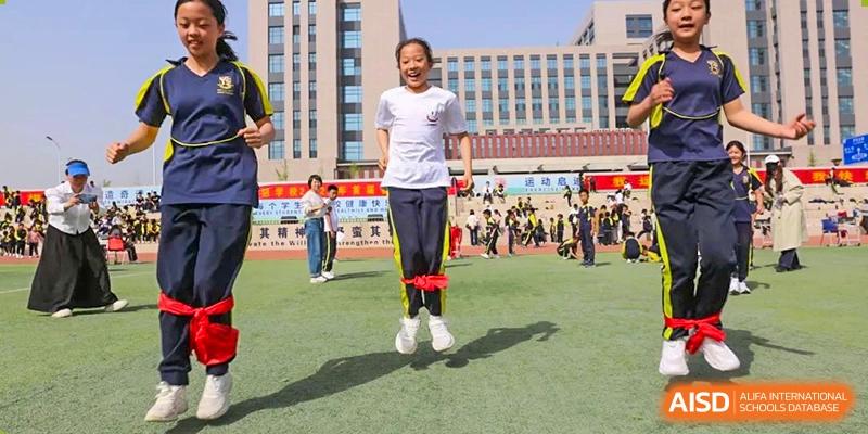 A female student smiling while successfully performing a double-leg skipping rope exercise on a green field, Brilliant Light School SJZ.