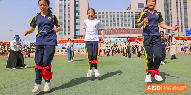 A female student smiling while successfully performing a double-leg skipping rope exercise on a green field, Brilliant Light School SJZ.
