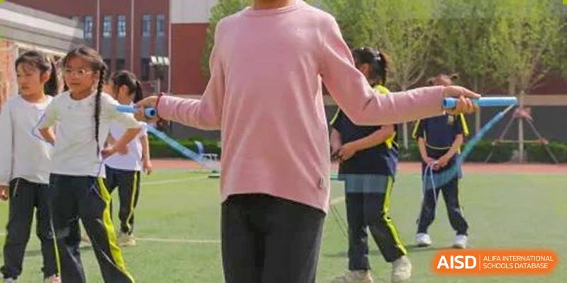 Close-up of a person in a pink shirt and black pants doing a jump rope exercise on a green field, Brilliant Light School SJZ.