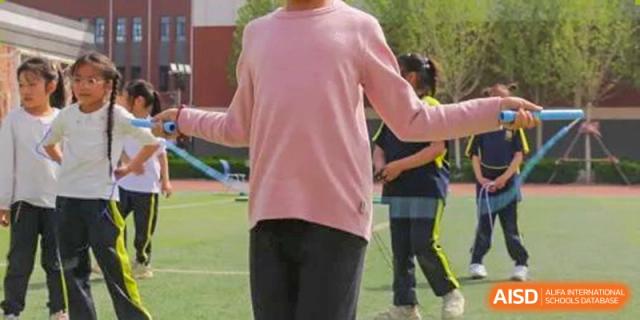Close-up of a person in a pink shirt and black pants doing a jump rope exercise on a green field, Brilliant Light School SJZ.