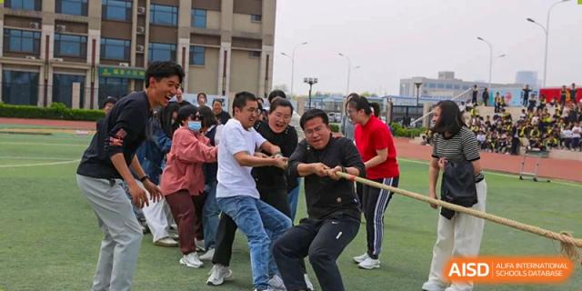 A group of students and adults participating in a tug-of-war competition outdoors, Brilliant Light School SJZ.