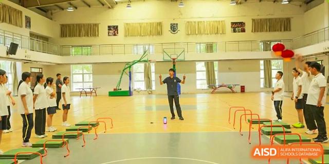 A teacher or coach demonstrating a sports activity in an indoor gymnasium with a basketball court, Brilliant Light School SJZ.