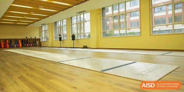 An empty, sunlit indoor gym or multi-purpose room with light wooden floors and large windows, Brilliant Light School SJZ.