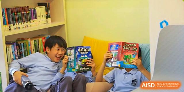 Two students smiling while holding and reading colorful books together in a brightly lit classroom at Britannica International School, Shanghai.