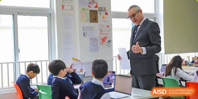 A teacher standing by a whiteboard with students seated and engaged in a collaborative project or discussion in a classroom at Britannica International School, Shanghai.