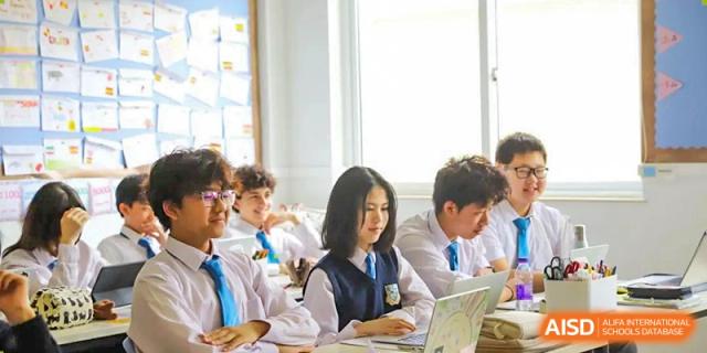 Older students in school uniform working on their laptops at a desk in a collaborative academic setting at Britannica International School, Shanghai.