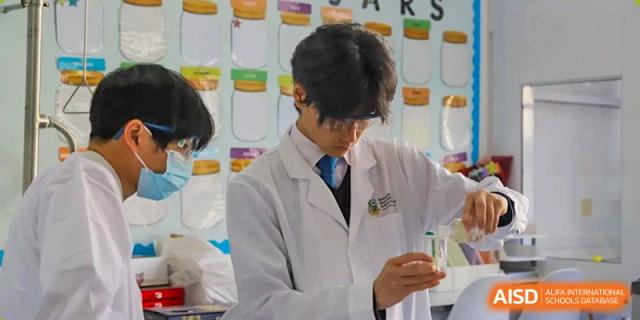 A male student wearing a white lab coat and holding a small vial during a practical experiment in the science laboratory at Britannica International School, Shanghai.