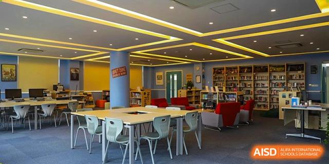 A modern, brightly lit library or comfortable student study area with tables, chairs, and books lining the walls at Britannica International School, Shanghai.