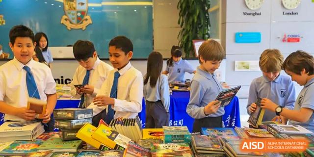 Students in school uniform browsing and selecting books at a book fair or book sale in an indoor school area at Britannica International School, Shanghai.