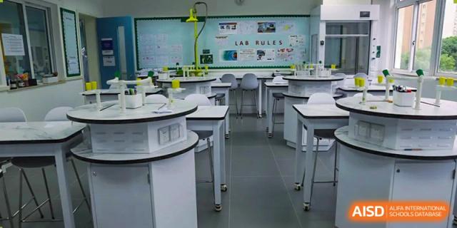 An empty, modern science laboratory classroom with white desks, stools, and a 'LAB RULES' board visible at Britannica International School, Shanghai.