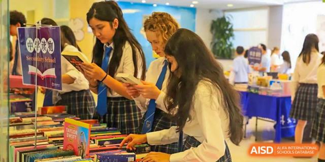 Three older students in school uniform working together and discussing materials at a desk in a collaborative study space at Britannica International School, Shanghai.