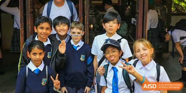 A close-up of a diverse group of four young students in uniform smiling and posing for a picture outdoors at Britannica International School, Shanghai.