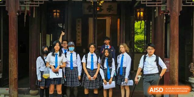 A group of students in uniform posing for a photo in front of a traditional Chinese wooden gate or entrance during a school trip or outing from Britannica International School, Shanghai.