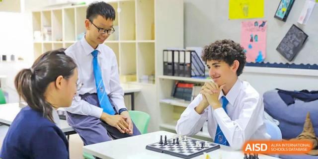 Two middle or high school students in uniform playing a game of chess in a classroom or common area at Britannica International School, Shanghai.