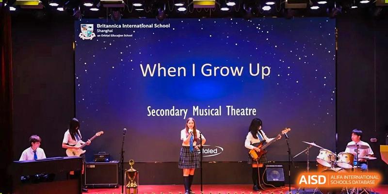 A student performing a song on stage under the banner "When I Grow Up Secondary Musical Theatre" at Britannica International School, Shanghai.