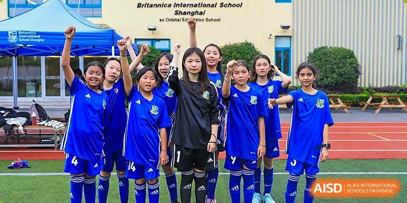 A group of girls in blue and black soccer uniforms posing for a team photo on the field at Britannica International School, Shanghai.