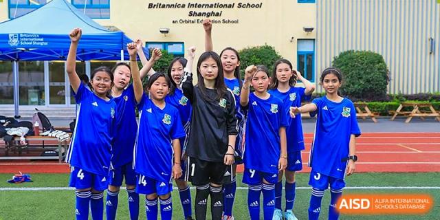 A group of girls in blue and black soccer uniforms posing for a team photo on the field at Britannica International School, Shanghai.