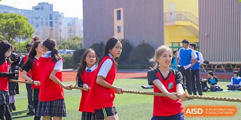 Students in red and white uniforms participating in a tug-of-war competition on a sports field at Britannica International School, Shanghai.