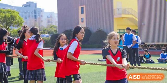 Students in red and white uniforms participating in a tug-of-war competition on a sports field at Britannica International School, Shanghai.