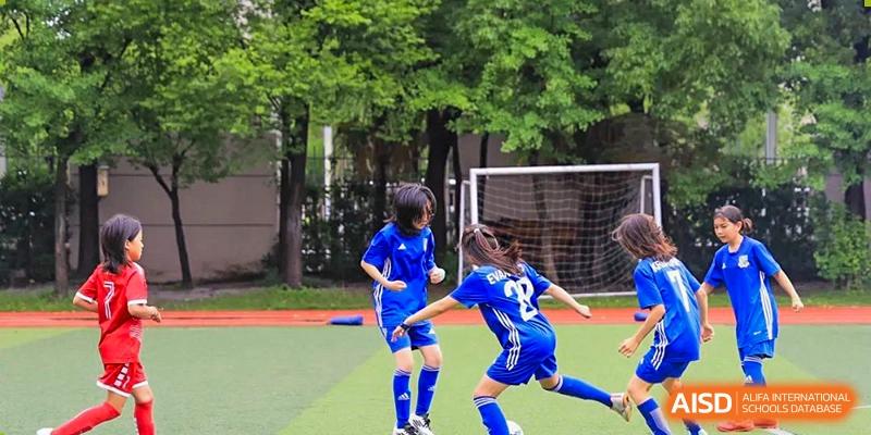 Two young students in blue soccer uniforms actively playing a game on the pitch with a goalpost visible in the background at Britannica International School, Shanghai.