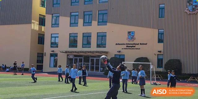 A group of students playing with a basketball-sized ball on the court in front of the main school building of Britannica International School, Shanghai.