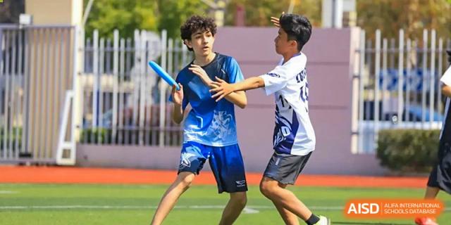 Close-up of students in blue and white sports uniforms running and vying for possession during a game on the sports field at Britannica International School, Shanghai.