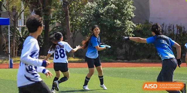 Two female students in sports uniforms passing a ball during a soccer or rugby game on a green field at Britannica International School, Shanghai.