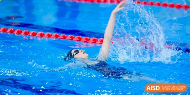 A student swimmer wearing goggles performing the freestyle stroke with their arm out of the water in a bright blue lane at Britannica International School, Shanghai.