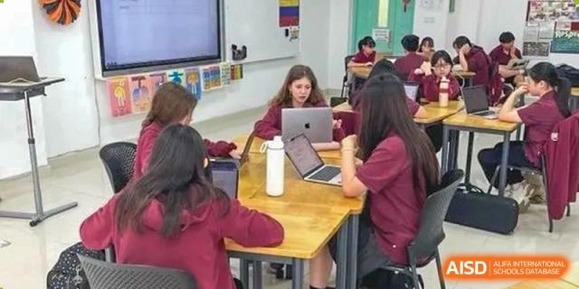Two female students working together on a project using a laptop at a table in a classroom at Canadian International School of Hefei.