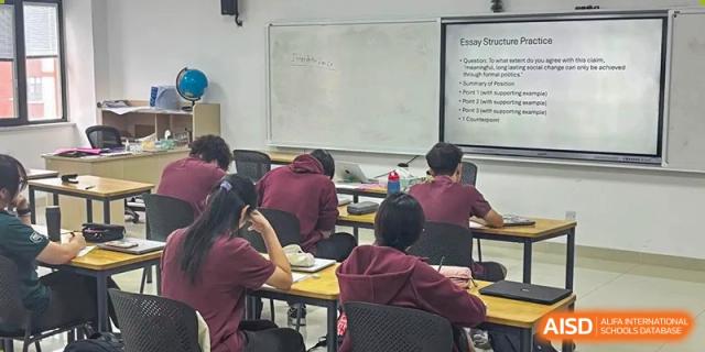 Students in burgundy uniforms sitting at desks, facing the whiteboard in a classroom during a lesson at Canadian International School of Hefei.
