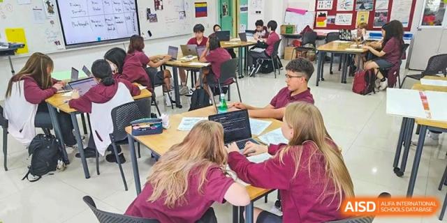 A group of four students collaborating at a desk using a laptop in a bright classroom setting at Canadian International School of Hefei.