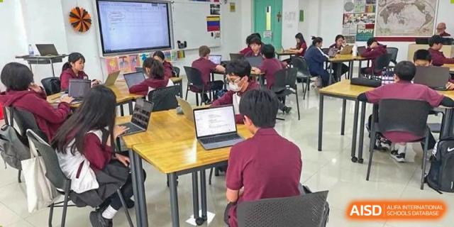 Students in uniforms sitting at tables, working on coding or text-based tasks displayed on their laptop screens at Canadian International School of Hefei.